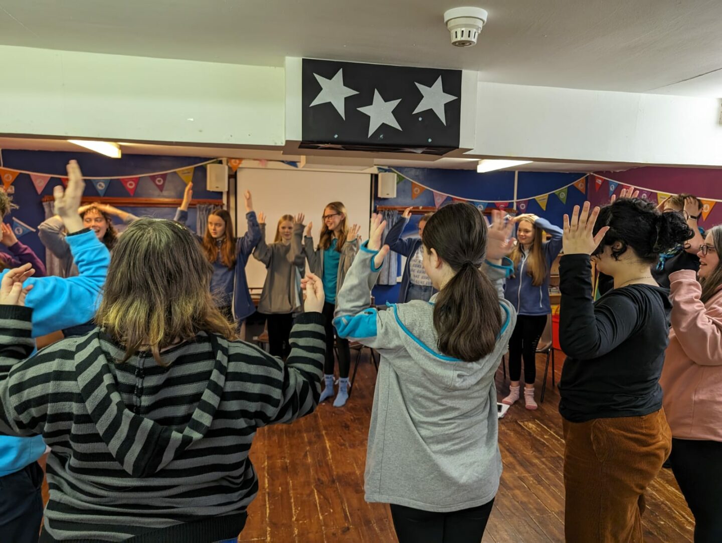 young members taking part in a peer education training day, stood in a circule with their hands by their heads