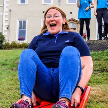 a photo of Sharon Weaver looking excited as she slides on a grass sledge down a hill