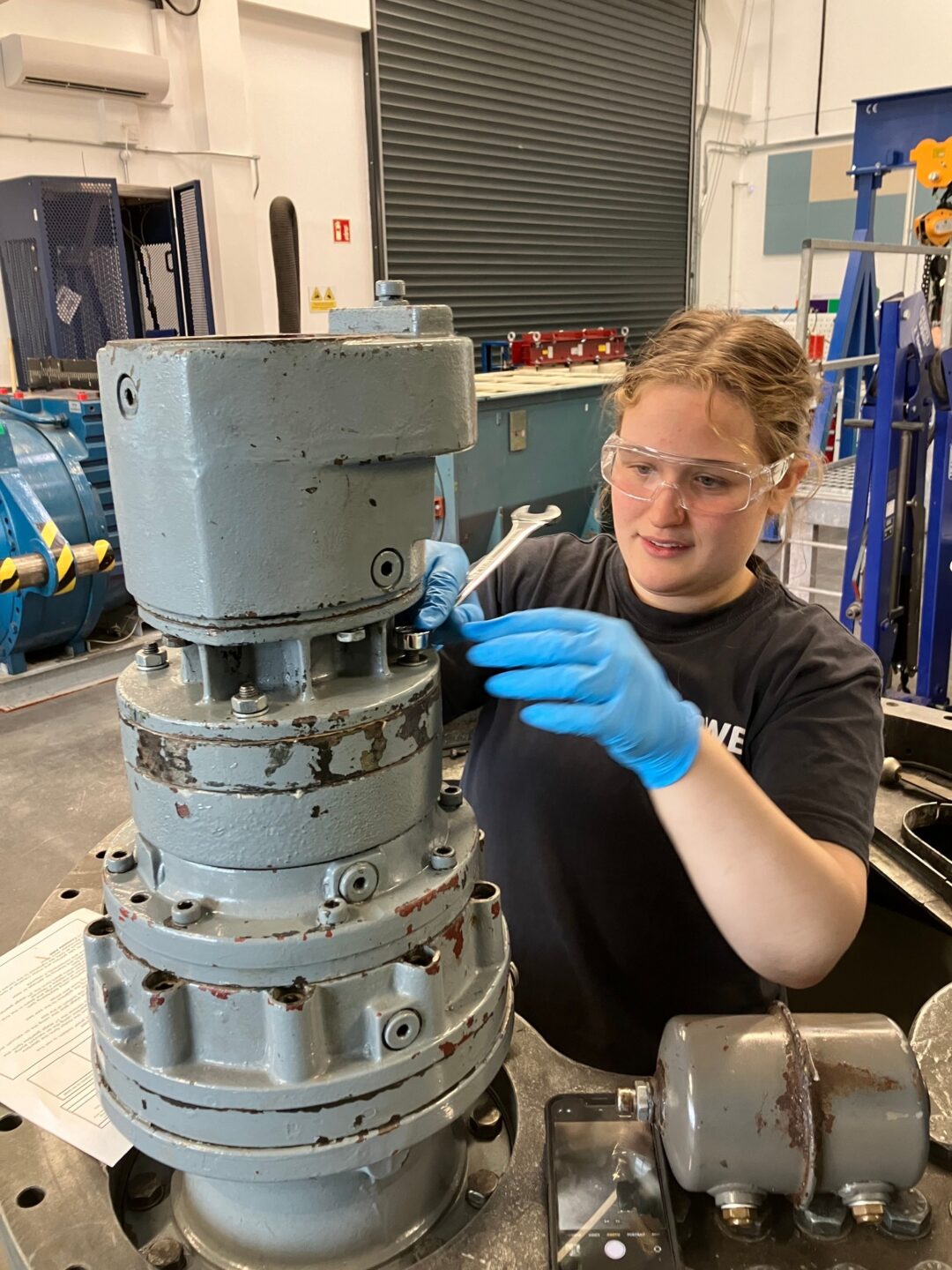Madeleine is shown at work. She is in an industrial setting working with machinery.